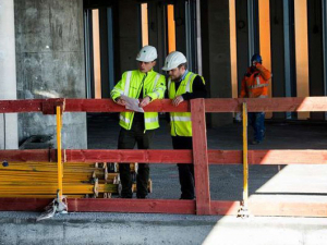 Two construction workers looking down in building construction site with wooden scaffolding around them.