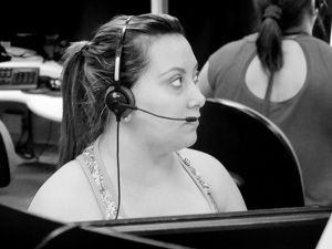 female call center worker with headset at cubicle, other workers in background