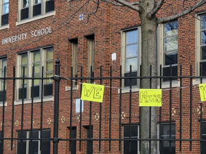 handwritten signs "we miss you" hang on the fence outside a brick building labeled Hartford University School