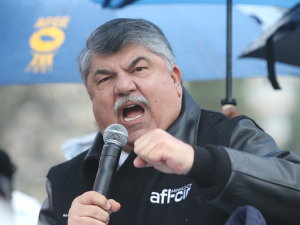 Richard Trumka speaking animatedly into a microphone, under an umbrella, at a 2016 demonstration.