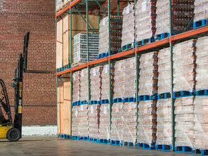 Worker with forklift in front of cases of pallets on shelves in warehouse