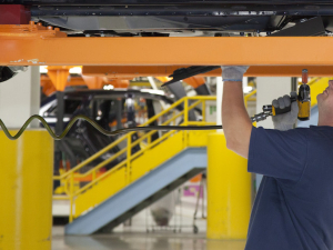 An autoworker tightens bolts on a car chassis above his head.