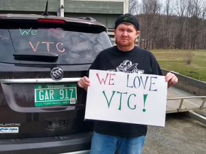 protester for VSCS Thrive! with a sign and his car that has a pro-VTU slogan on the back windshield