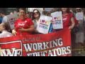 Three women mostly in red shirts looking at the camera hold signs saying “Love Wins,” and a red banner with outlined white lettering saying “Caucus of Working Educators.” 