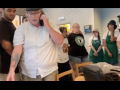 Starbucks workers in aprons surround a manager in a white shirt, the manager is leaving and talking on the phone
