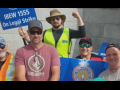 Five men in hats, sunglasses and hi-viz vests hold signs--including one that says IBEW 1555 On Legal Strike