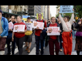 Eight people walk towards the camera, three with signs that say, “shame, Russel Vought”