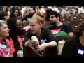 Two women talk across seats in filled auditorium.