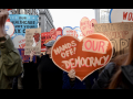 A heart-shaped sign saying “Hands Off Our Democracy” is carried in a crowd.