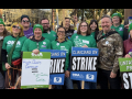 A group of green-shirted union members hold strike signs and smile.