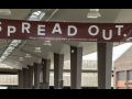 SPREAD OUT written on a sign above a road with pillars in the background.