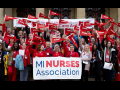 Large crowd of Michigan Nurses Association members posing in red with flags and banner on steps assembled.