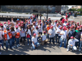 A group of fifty workers red hats and white shirts raise their fists and pose for the camera