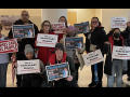 A group of 10 people inside hold signs saying “Nurses Care for All People” and “transgender rights are human rights” 