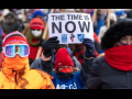 Marchers bundled in coats, one carries printed sign: "The time is now!"