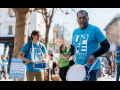 Two men in blue shirts that say “UPTE” play snare drums while others march in the background.