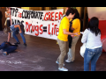 Activists draw chaik outlines on the ground in front of a hotel entrance; one outline is labeled "Vietnam." Others hold a banner: "TPP is corporate greed. AiDS drugs = life." 