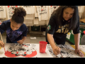 A child and an adult paint signs. Behind them are many more signs hanging already painted.