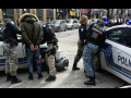 Outdoors, four police officers handcuffing two people against two police cars