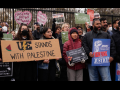 A chanting crowd stands in front of the White House fence. Three people are helping hold a large cardboard sign that says "UE stands with Palestine" with the union's lightning-bolt logo and a slice of watermelon. Other printed signs say "American Postal Workers Union: Fighting for Justice" and "Biden, you are starving Gaza. Permanent ceasefire now!" 