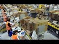 Amazon warehouse with goods on shelves and workers in orange vests working.