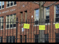 handwritten signs "we miss you" hang on the fence outside a brick building labeled Hartford University School