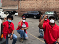 Four Black workers in red Verizon shirts kneel in a parking lot, fists raised.