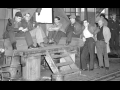 A group of autoworkers sit on a makeshift platform under a window in a factory.