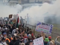 A dense cloud of tear gas envelops a crowd with colorful signs.