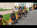 Workers in Italy sitting outside a warehouse on strike in orange vests.