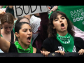 Two women in green bandanas that say “bans off our bodies” march with many others