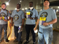 Four men of various races in blue UAWD shirts face the camera holding one-member one-vote fliers.