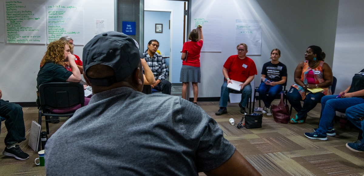 A group of labor activists sit together in a room while one writes ideas on a piece of flip chart paper on the wall.