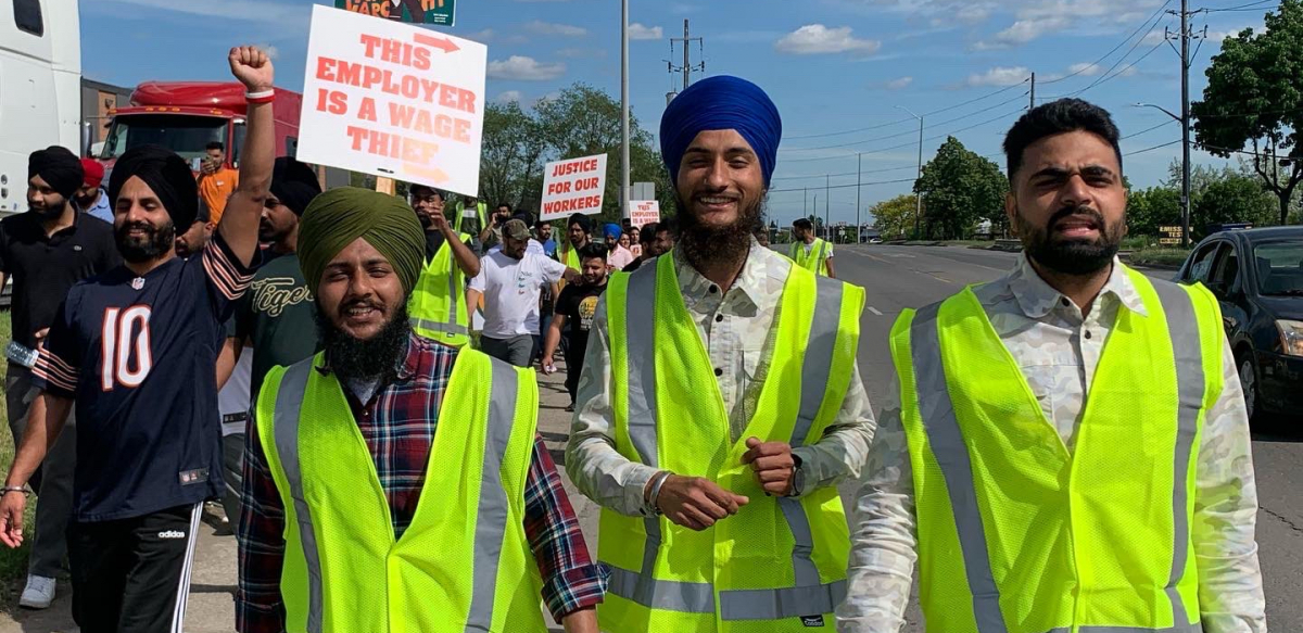 Members of the Naujawan Support Network march holding signs that say "This employer is a wage thief."