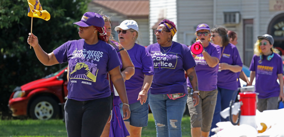 A group of black and white workers wearing purple SEIU T-shirts march.