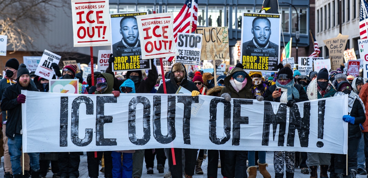 A big crowd carries a banner “ICE out of MN!”
