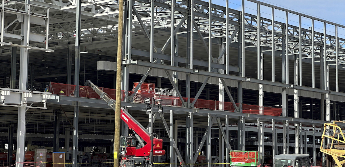 Metal ribs and girders of a factory being constructed are visible, with a red construction crane