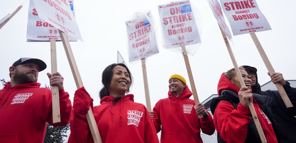 Five women and men in red hoodies that say “strike strike strike” hold picket signs