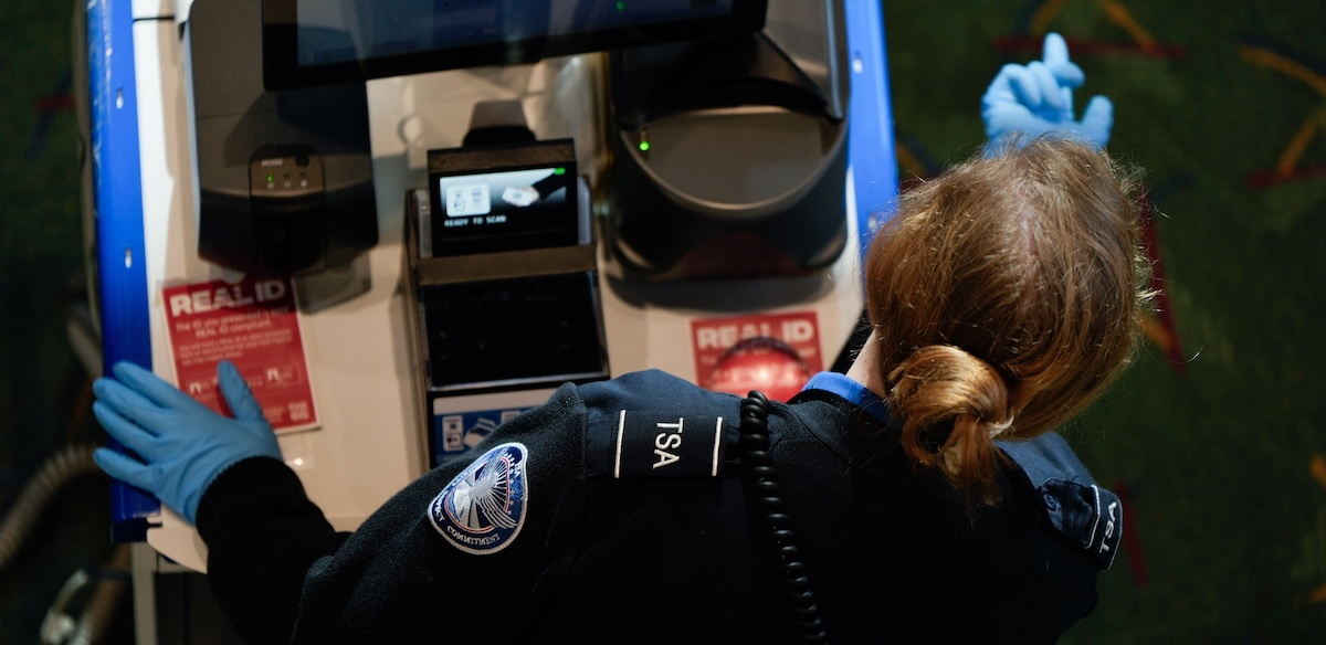 A TSA worker, seen over her shoulder, motions a passenger forward with a blue gloved finger