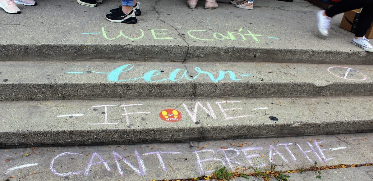 Steps chalked in blue and pink with the words we can't learn if we can't breathe with a few students feet and shoes visible