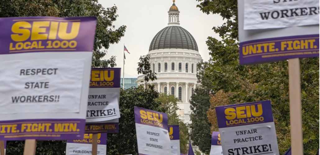 Printed SEIU Local 1000 picket signs reading "Respect state workers!!" and "Unfair practice strike!" are raised aloft with a capitol rotunda visible behind them.