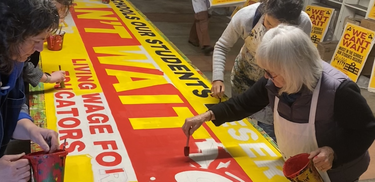 Several people paint a big banner that says ‘We Can’t Wait.’