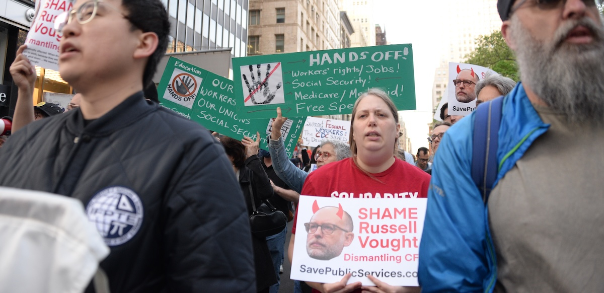 Several workers with signs march towards the camera.  Some say “Hands Off” our workers, our union, Social Security and other items