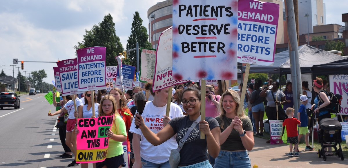 A group of nurses hold picket signs by a street