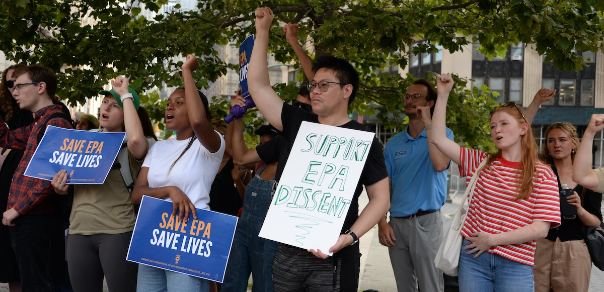 Several people raise their fists, one holds a homemade sign saying “support EPA dissent”