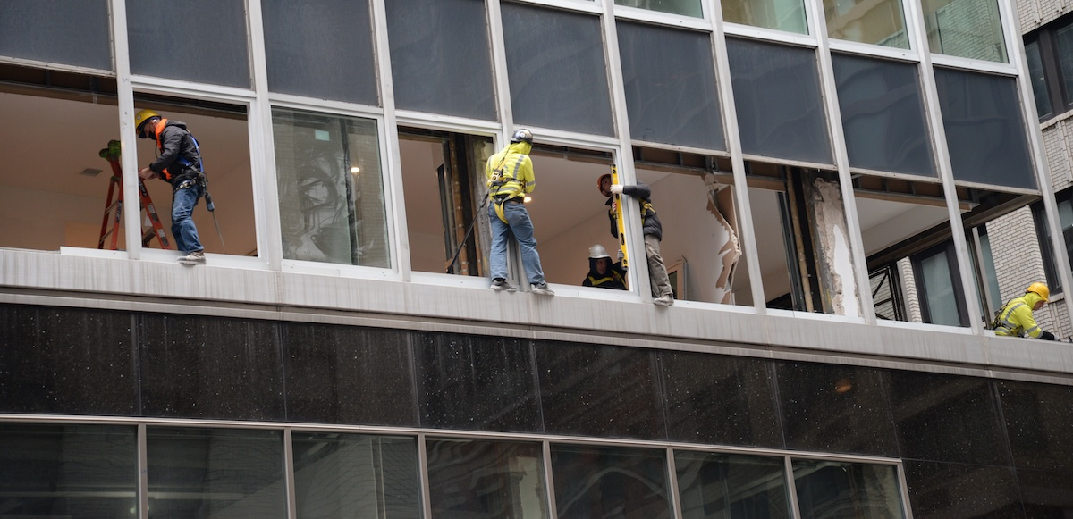Workers in harnesses work outside windows doing construction.