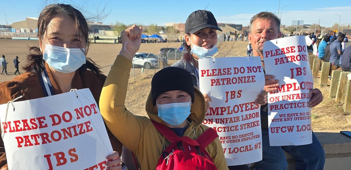 Four strikers holding signs, one with a fist in the air, face the camera.