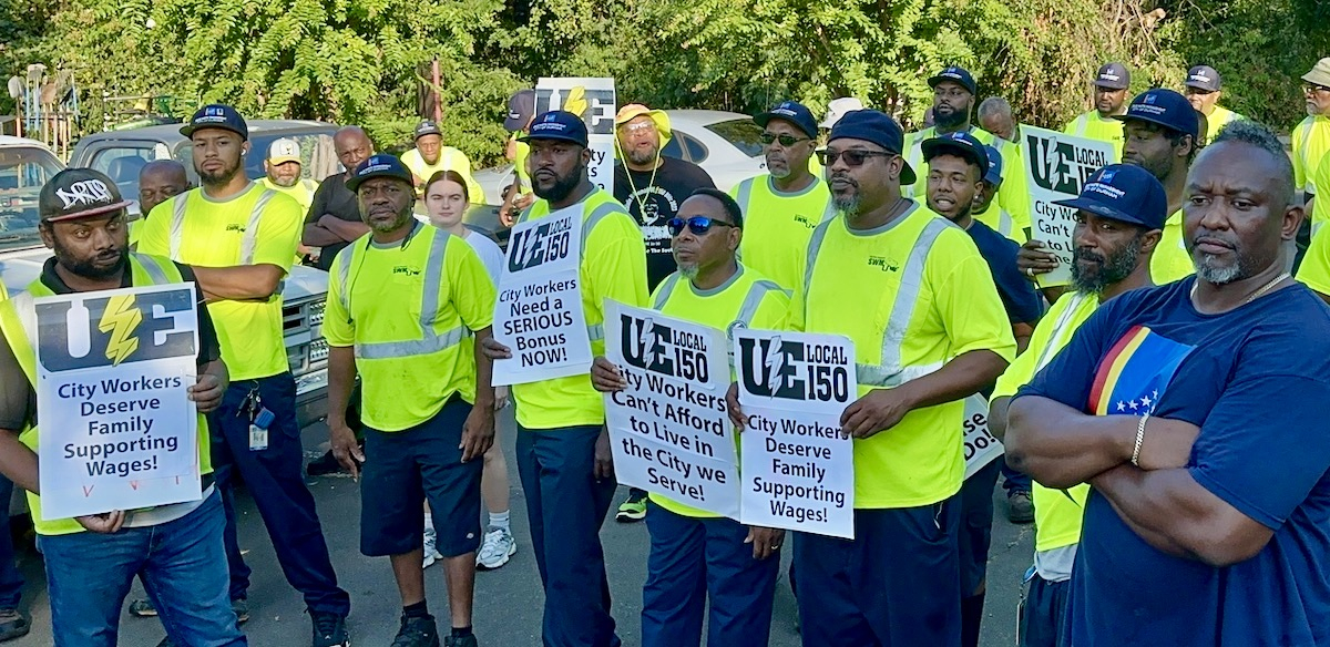 A group of Black men in hi viz green shirts hold signs saying “City workers demand family supporting wages”