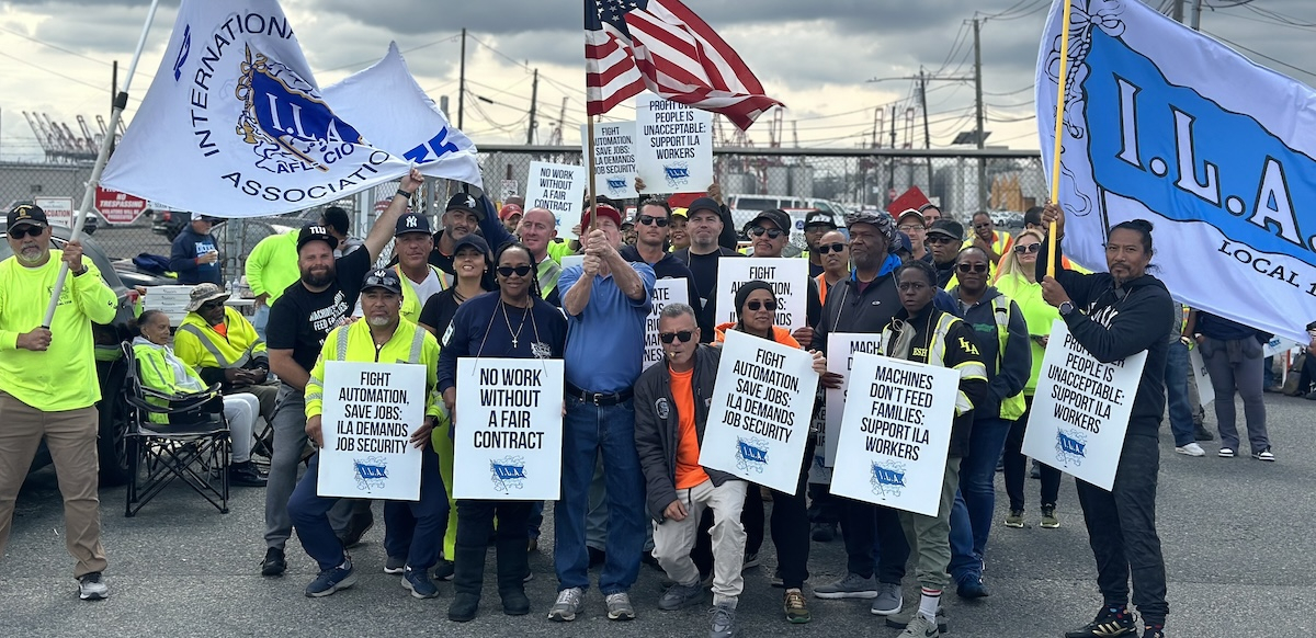 Thirty workers with ILA flags line up for the camera, smiling and waving signs
