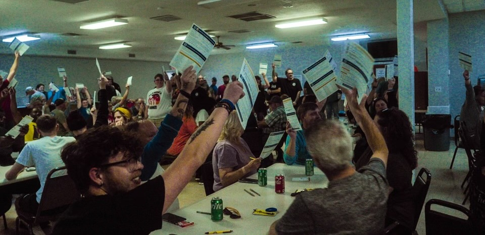 60 people at tables hold papers high in the air